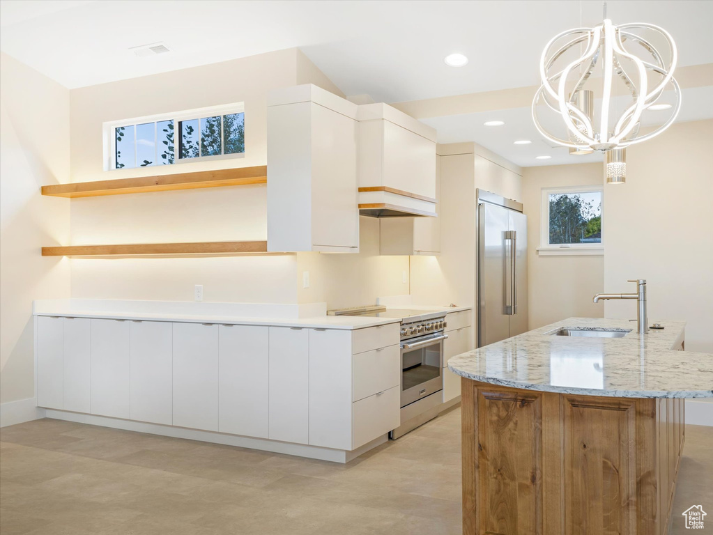 Kitchen with premium appliances, a center island with sink, open shelves, a sink, and light stone countertops