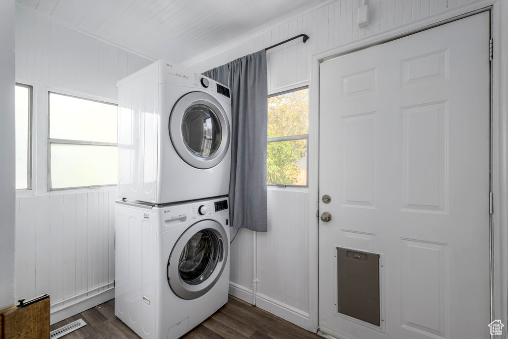 Laundry area with wood walls, stacked washing maching and dryer, and dark wood-type flooring