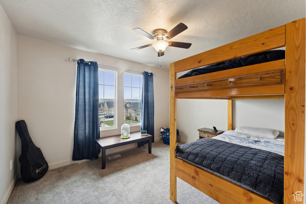 Carpeted bedroom with ceiling fan and a textured ceiling