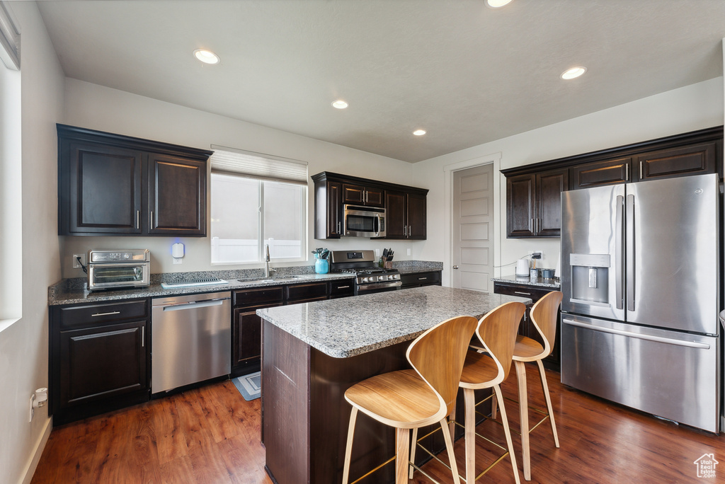 Kitchen with appliances with stainless steel finishes, dark hardwood / wood-style floors, stone counters, sink, and a center island