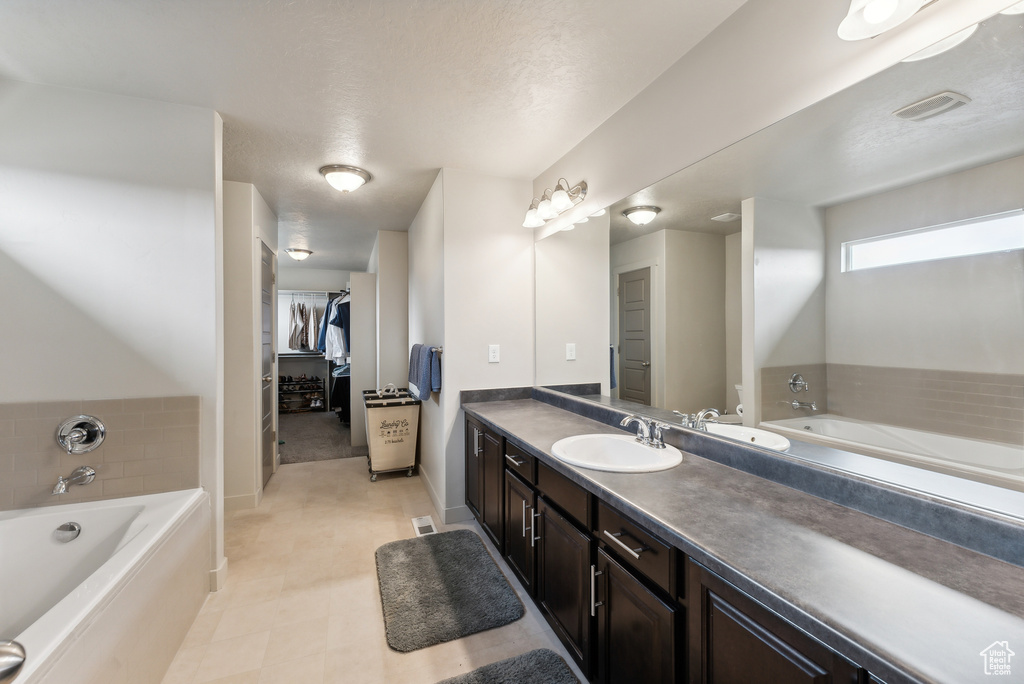 Bathroom with vanity, a textured ceiling, and a relaxing tiled tub