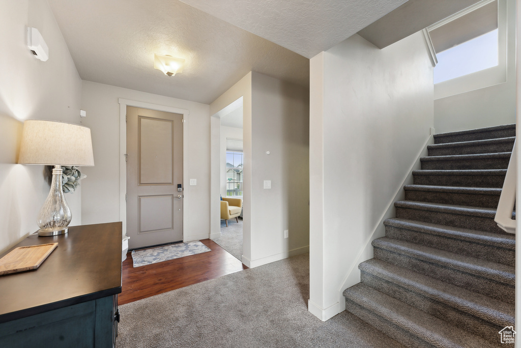 Foyer entrance featuring a textured ceiling and dark colored carpet