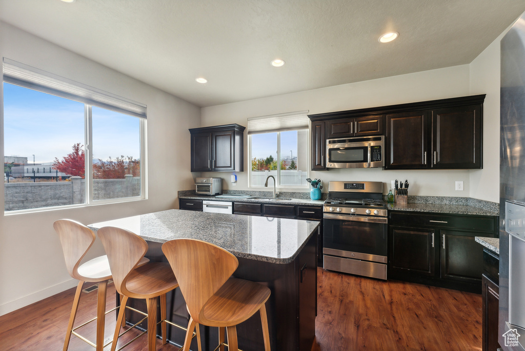 Kitchen with dark hardwood / wood-style floors, stainless steel appliances, sink, light stone countertops, and a center island