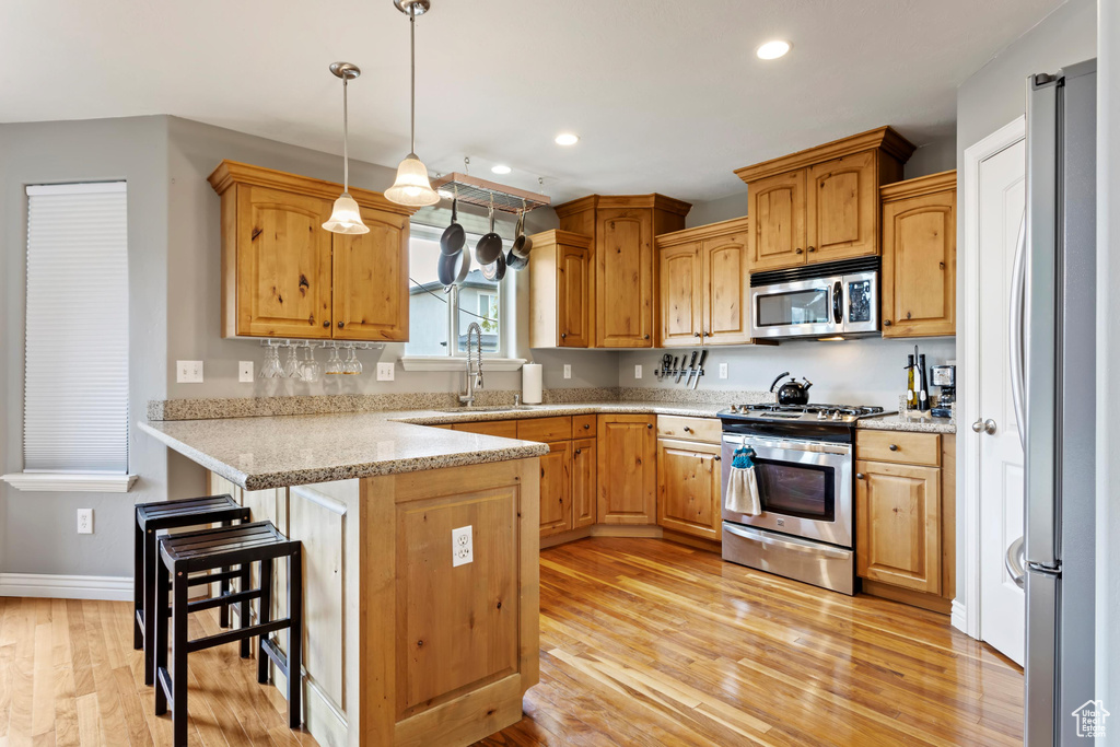 Kitchen featuring hanging light fixtures, stainless steel appliances, kitchen peninsula, sink, and light hardwood / wood-style floors