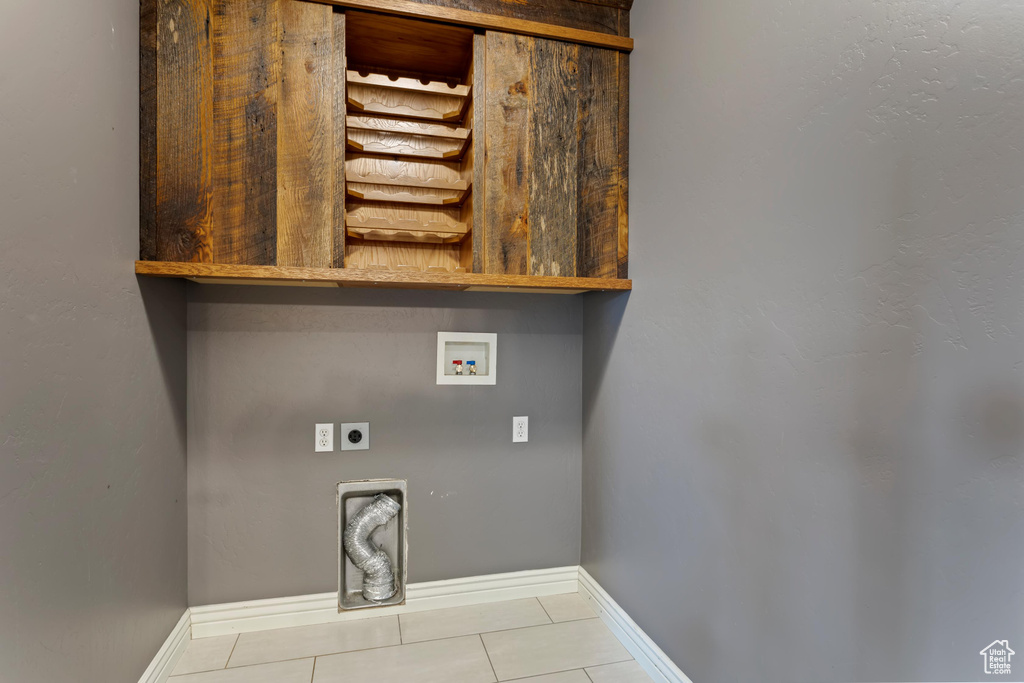 Clothes washing area featuring electric dryer hookup, tile patterned flooring, cabinets, and hookup for a washing machine