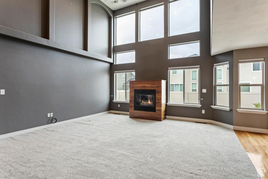 Unfurnished living room featuring a towering ceiling, wood-type flooring, and plenty of natural light