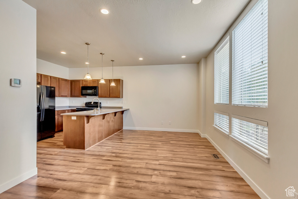 Kitchen with a breakfast bar area, kitchen peninsula, black appliances, pendant lighting, and light wood-type flooring