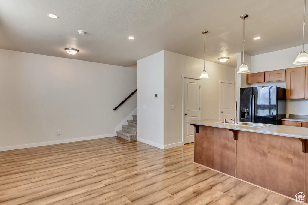 Kitchen with black refrigerator with ice dispenser, light hardwood / wood-style flooring, hanging light fixtures, and a breakfast bar