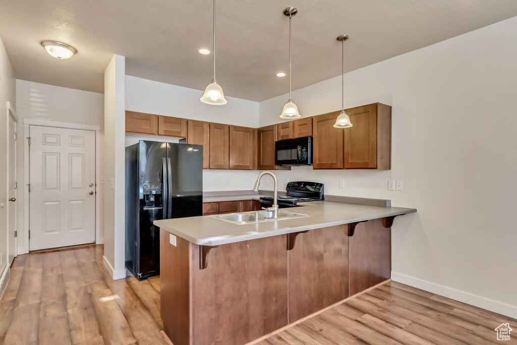 Kitchen featuring kitchen peninsula, light hardwood / wood-style flooring, black appliances, pendant lighting, and sink