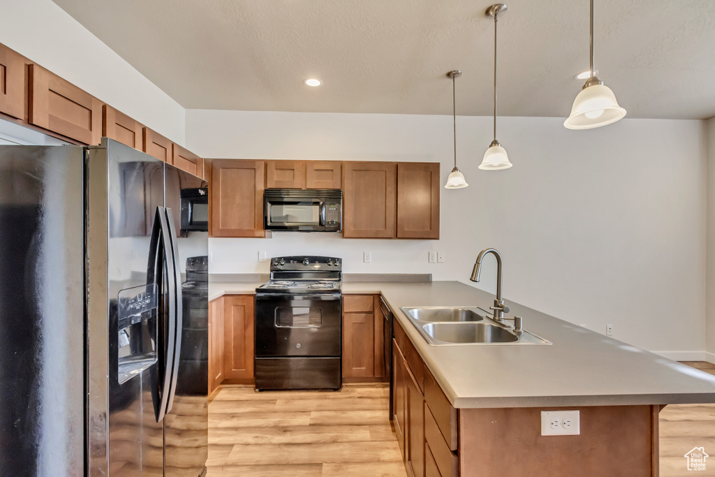 Kitchen with black appliances, sink, light wood-type flooring, kitchen peninsula, and decorative light fixtures