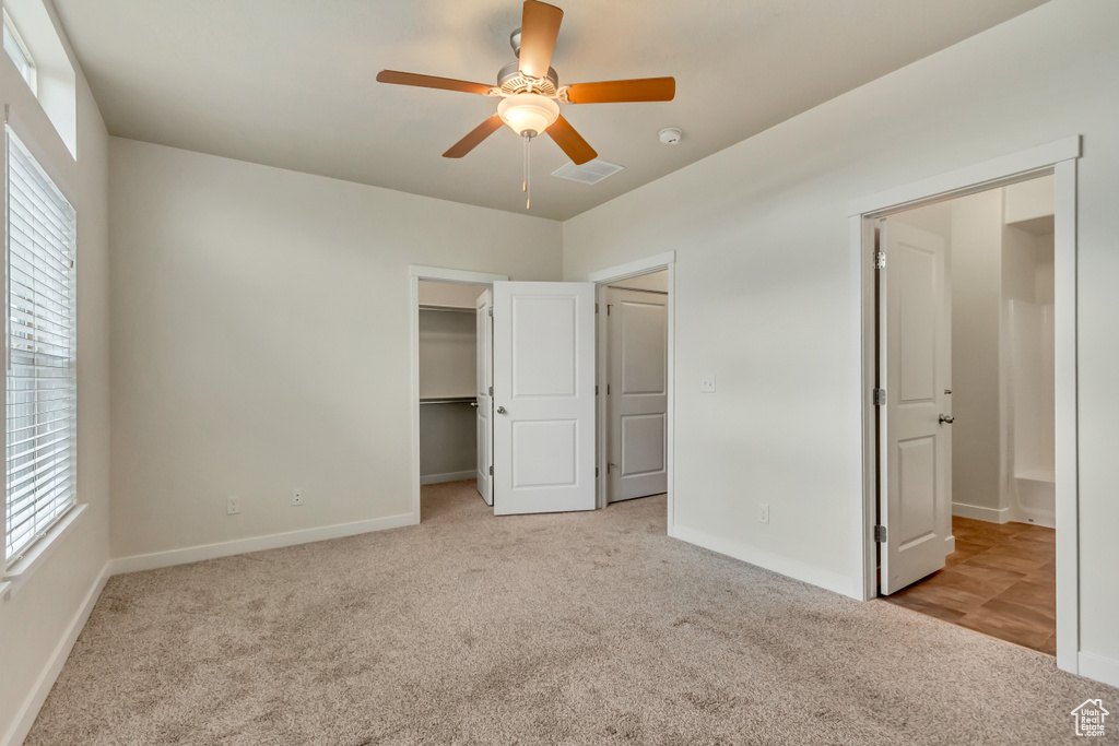 Unfurnished bedroom with ceiling fan, a walk in closet, and light colored carpet