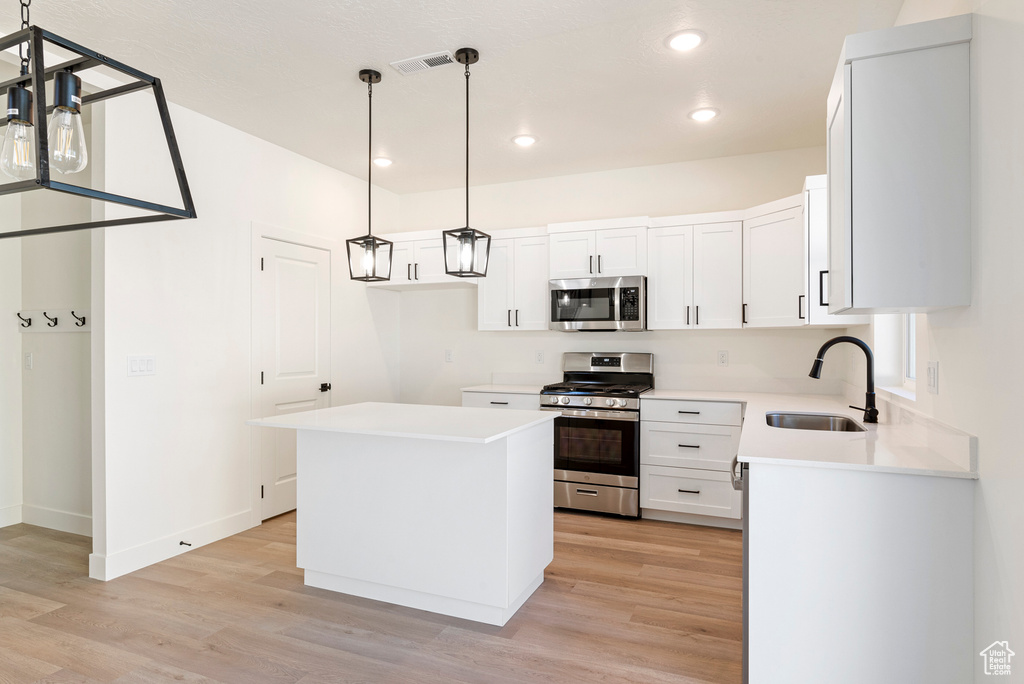 Kitchen featuring a kitchen island, sink, white cabinets, light wood-type flooring, and appliances with stainless steel finishes