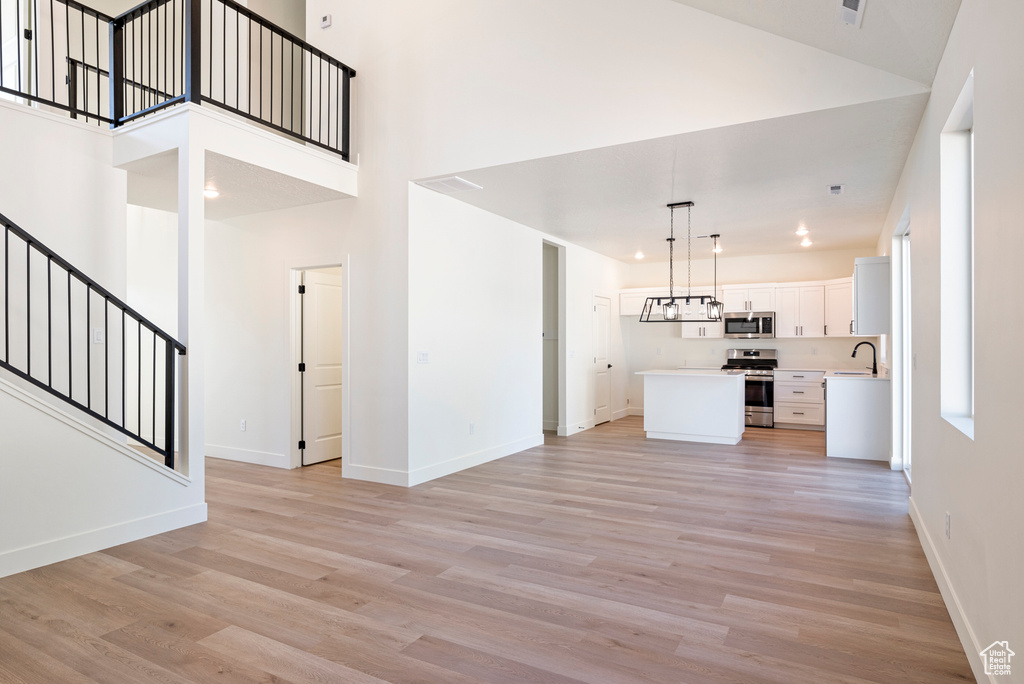 Unfurnished living room with a towering ceiling, sink, an inviting chandelier, and light hardwood / wood-style floors