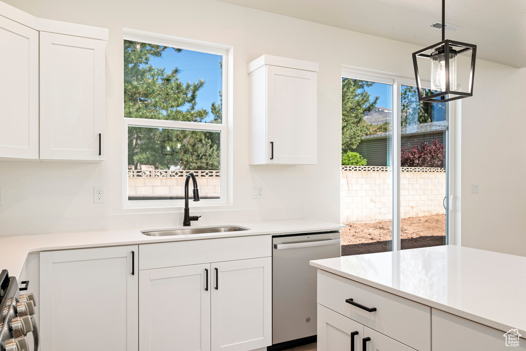 Kitchen featuring stainless steel appliances, sink, decorative light fixtures, an inviting chandelier, and white cabinetry