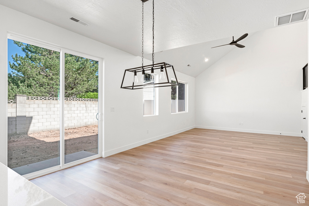 Unfurnished dining area with light hardwood / wood-style floors, a textured ceiling, vaulted ceiling, and ceiling fan