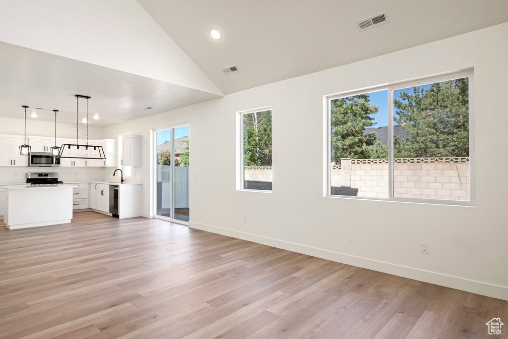 Unfurnished living room with lofted ceiling, sink, and light wood-type flooring