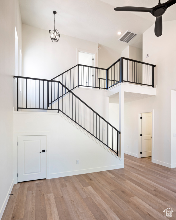 Stairs with ceiling fan with notable chandelier, hardwood / wood-style flooring, and a towering ceiling