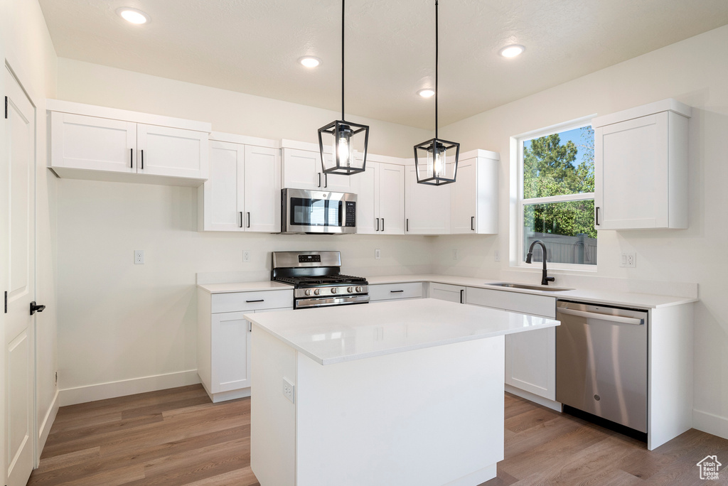 Kitchen with hanging light fixtures, white cabinetry, stainless steel appliances, sink, and a center island