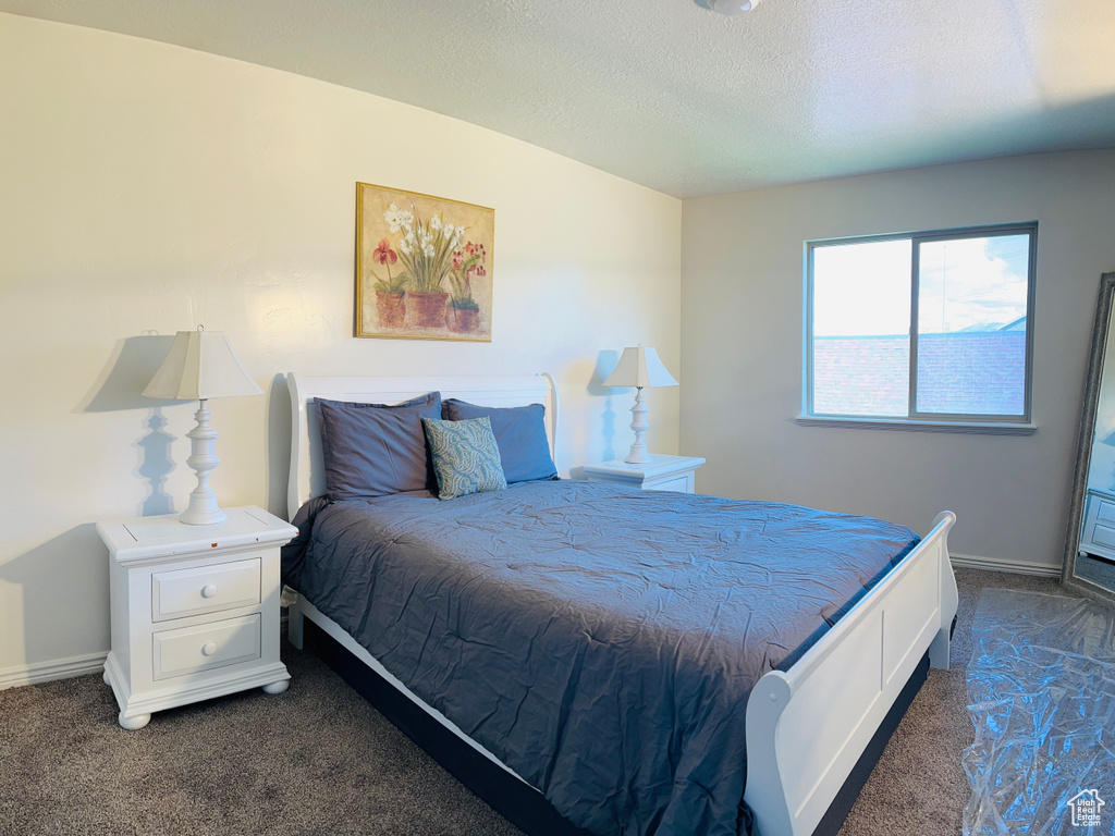 Bedroom featuring a textured ceiling, baseboards, and dark carpet