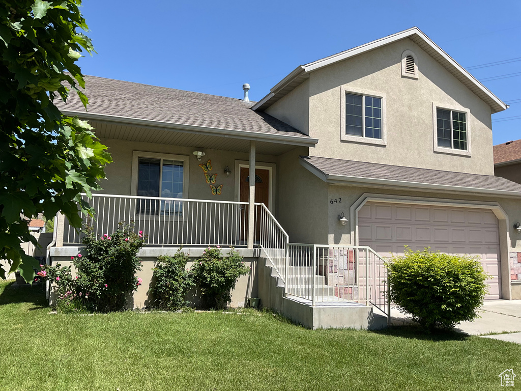 View of front of house with stucco siding, a garage, a front yard, covered porch, and a shingled roof
