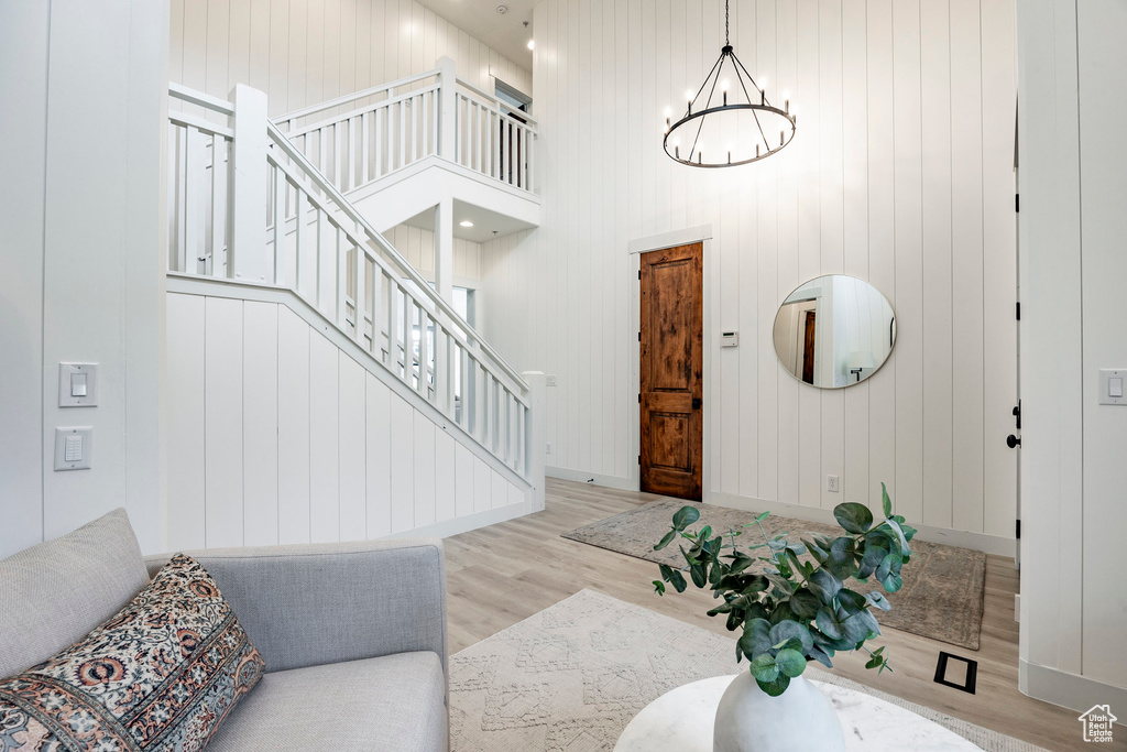 Foyer entrance featuring light hardwood / wood-style flooring, wooden walls, a notable chandelier, and a high ceiling