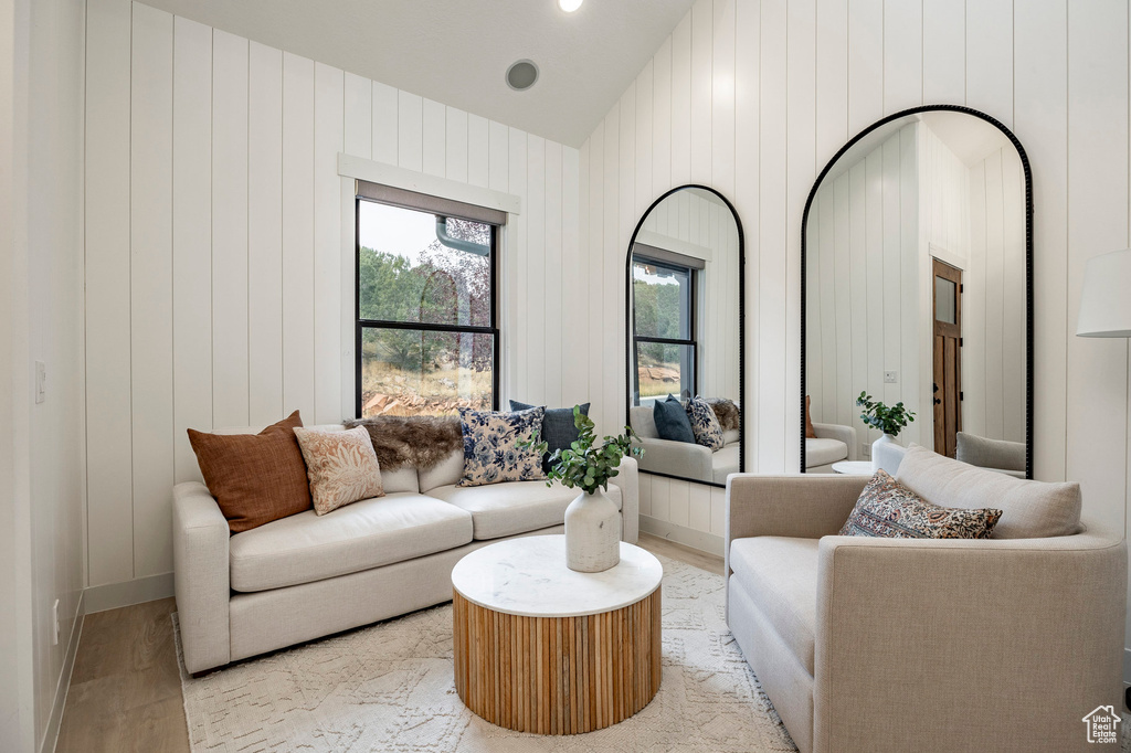 Living room with wooden walls, high vaulted ceiling, and light hardwood / wood-style floors