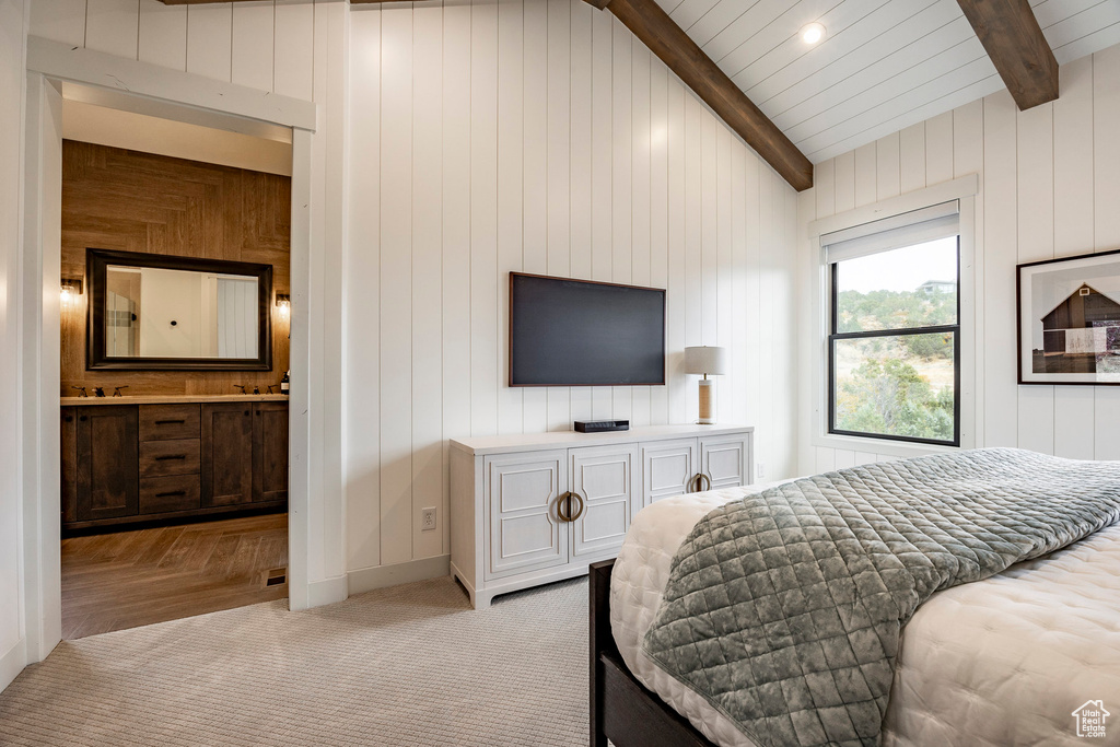 Bedroom featuring connected bathroom, vaulted ceiling with beams, sink, wooden walls, and light parquet floors