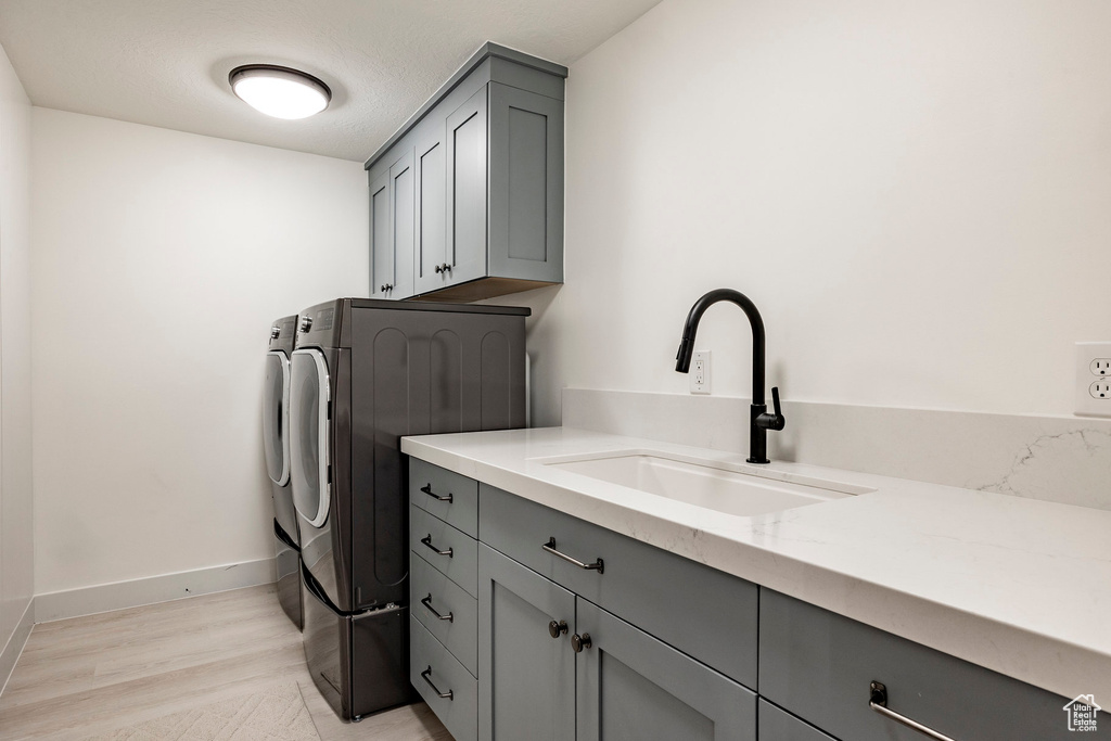 Washroom featuring sink, washing machine and clothes dryer, light hardwood / wood-style floors, and cabinets