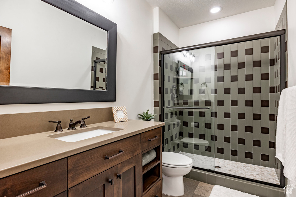 Bathroom featuring vanity, a shower with shower door, toilet, and tile patterned flooring