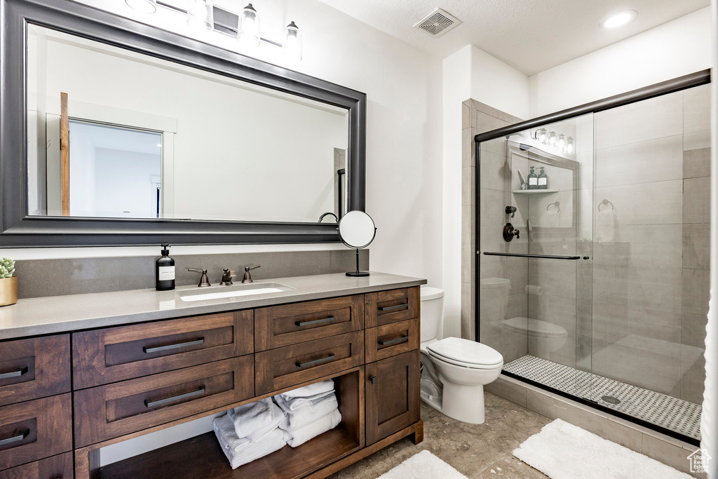 Bathroom with vanity, a shower with shower door, and toilet