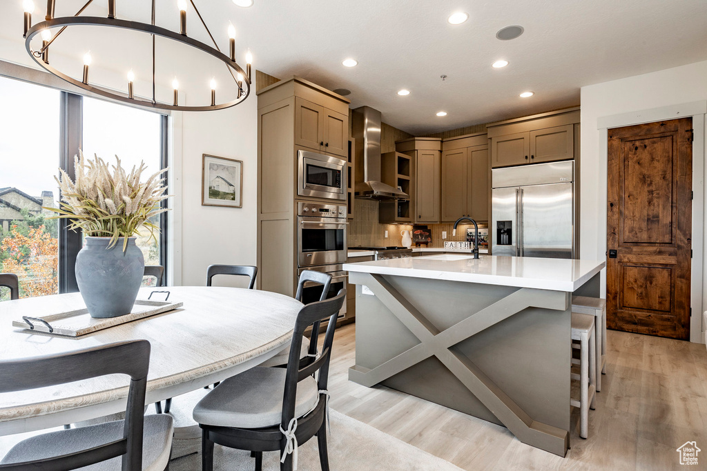 Kitchen with built in appliances, a healthy amount of sunlight, wall chimney exhaust hood, and hanging light fixtures