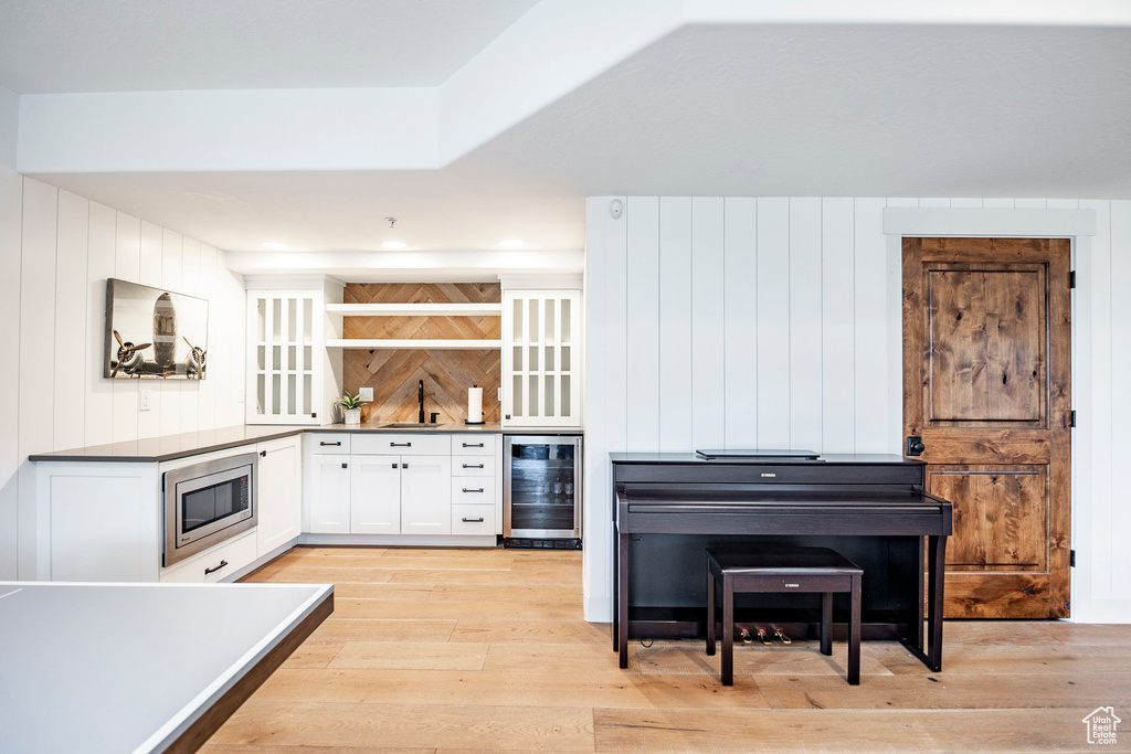 Kitchen with white cabinets, beverage cooler, stainless steel microwave, light wood-type flooring, and sink