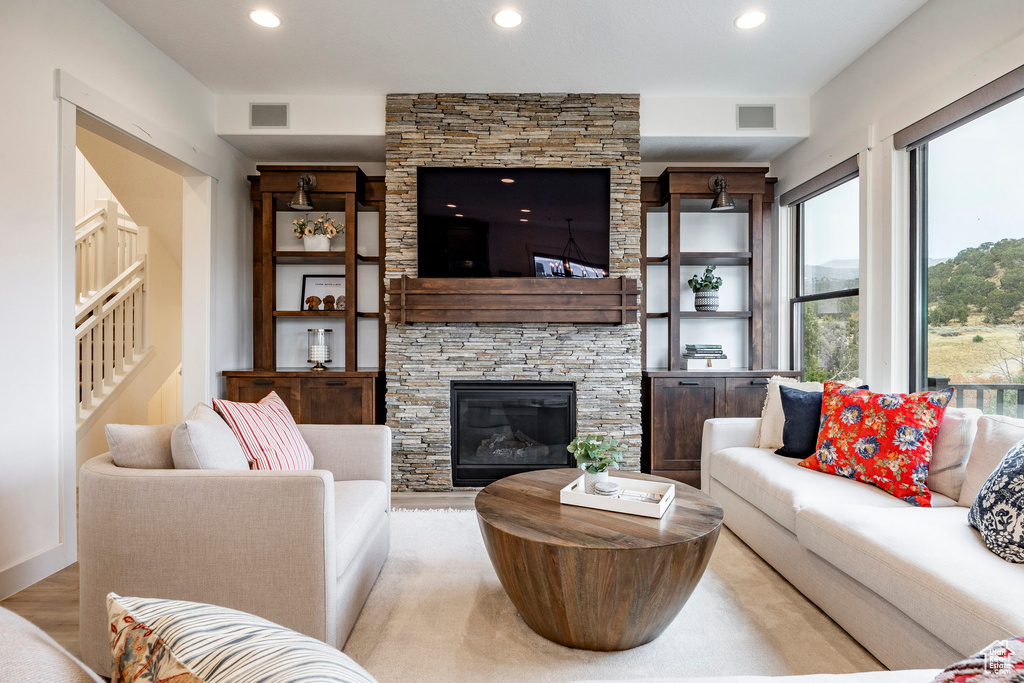 Living room with plenty of natural light, a stone fireplace, and light wood-type flooring