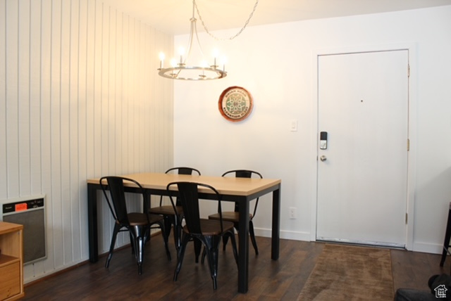 Dining area with dark wood-type flooring, an inviting chandelier, and wooden walls