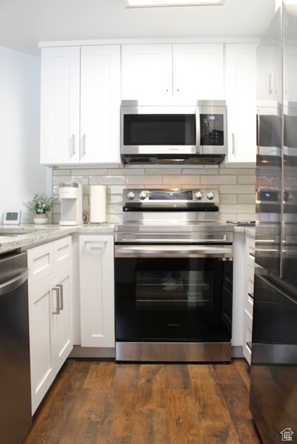 Kitchen with white cabinets, tasteful backsplash, dark hardwood / wood-style flooring, appliances with stainless steel finishes, and light stone counters