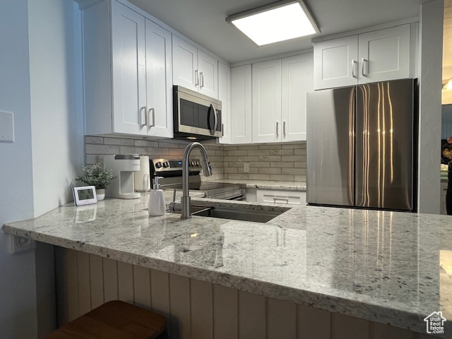 Kitchen with decorative backsplash, white cabinetry, light stone countertops, and stainless steel appliances