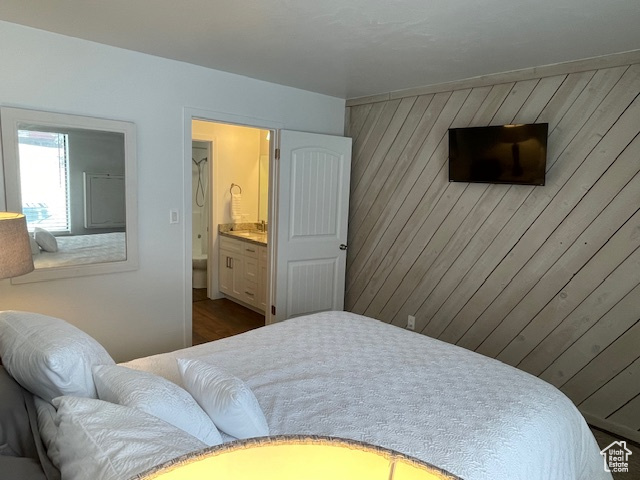 Bedroom with ensuite bathroom, wood walls, and dark hardwood / wood-style flooring