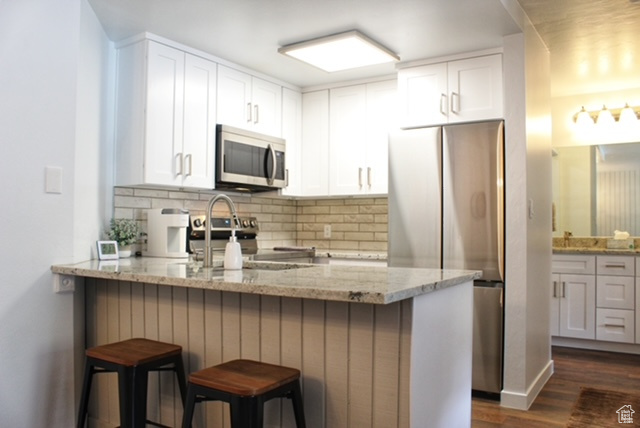 Kitchen featuring stainless steel appliances, white cabinets, dark wood-type flooring, light stone counters, and a breakfast bar