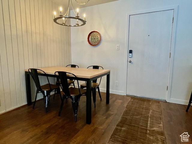 Dining area with wood walls, a chandelier, and dark wood-type flooring