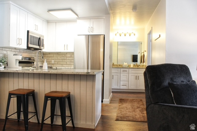 Kitchen with white cabinets, a kitchen bar, dark hardwood / wood-style floors, stainless steel appliances, and light stone counters