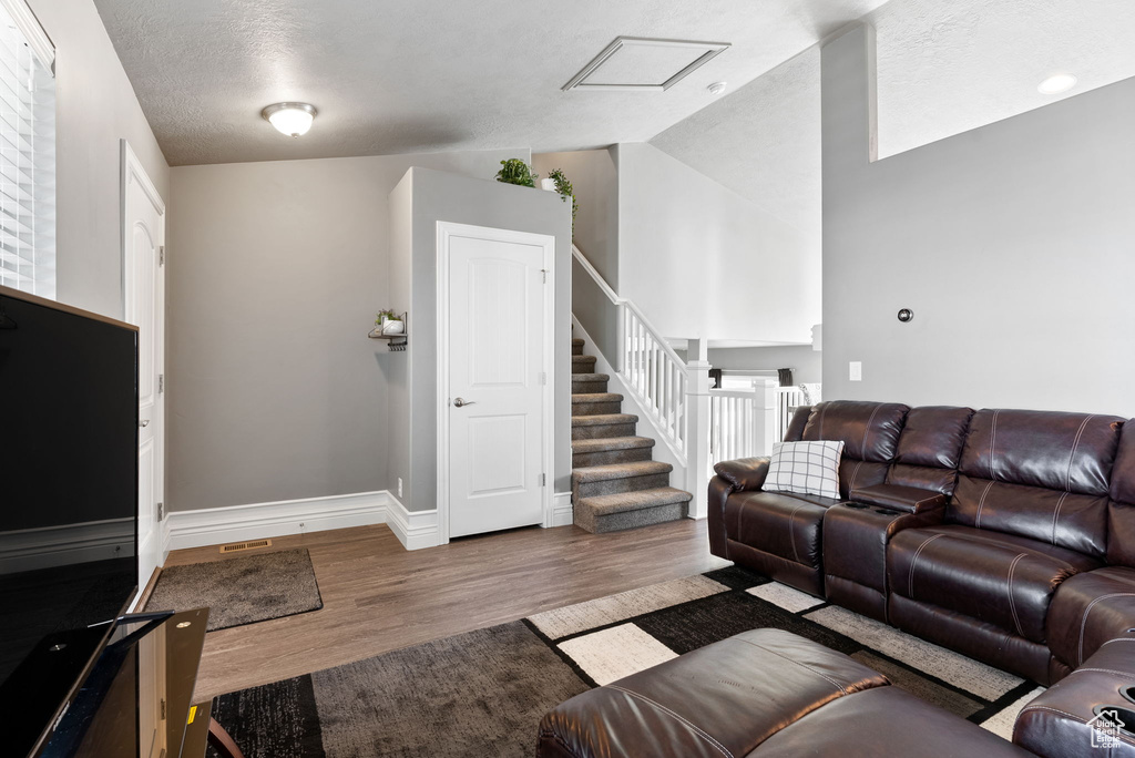 Living room with a textured ceiling, vaulted ceiling, and wood-type flooring