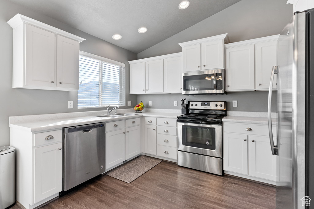 Kitchen featuring appliances with stainless steel finishes, lofted ceiling, dark hardwood / wood-style floors, and white cabinets