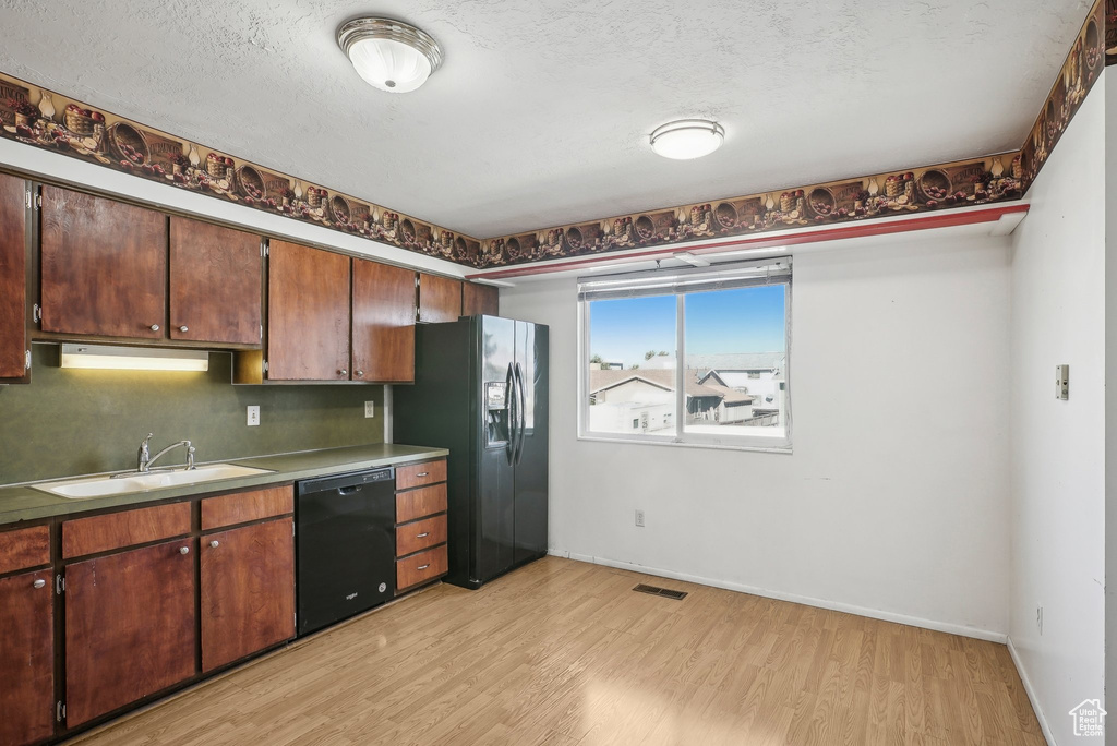 Kitchen with light hardwood / wood-style floors, a textured ceiling, black appliances, and sink