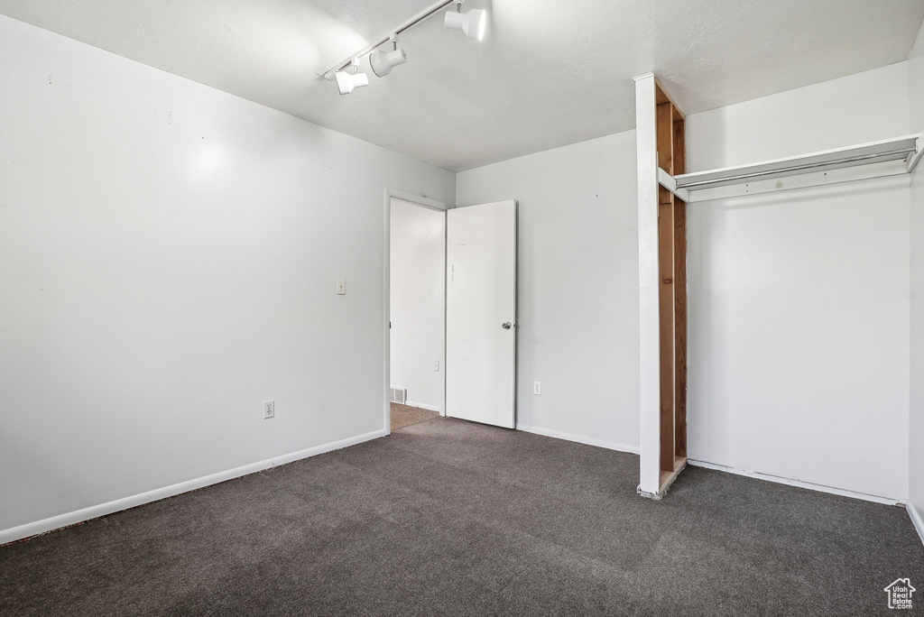 Unfurnished bedroom with a closet, dark carpet, and rail lighting