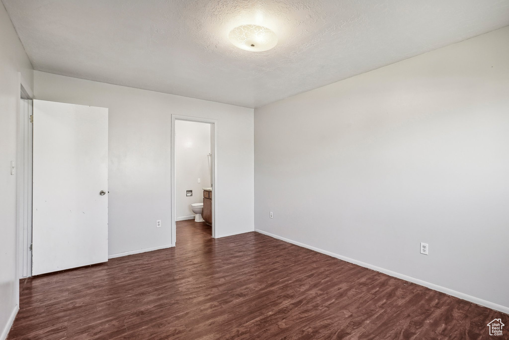 Unfurnished bedroom featuring connected bathroom, dark wood-type flooring, and a textured ceiling