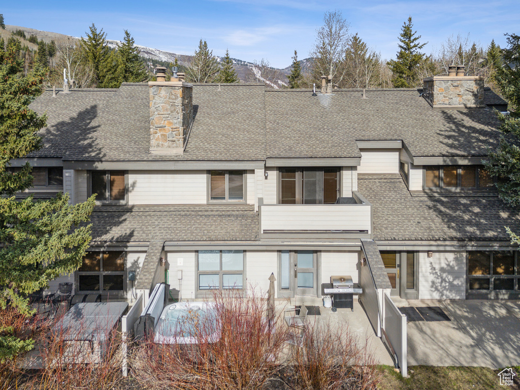 Back of property with a shingled roof, a mountain view, a chimney, and a patio area
