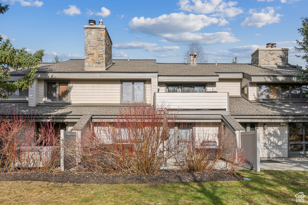 Back of property with a shingled roof, a chimney, and a garage