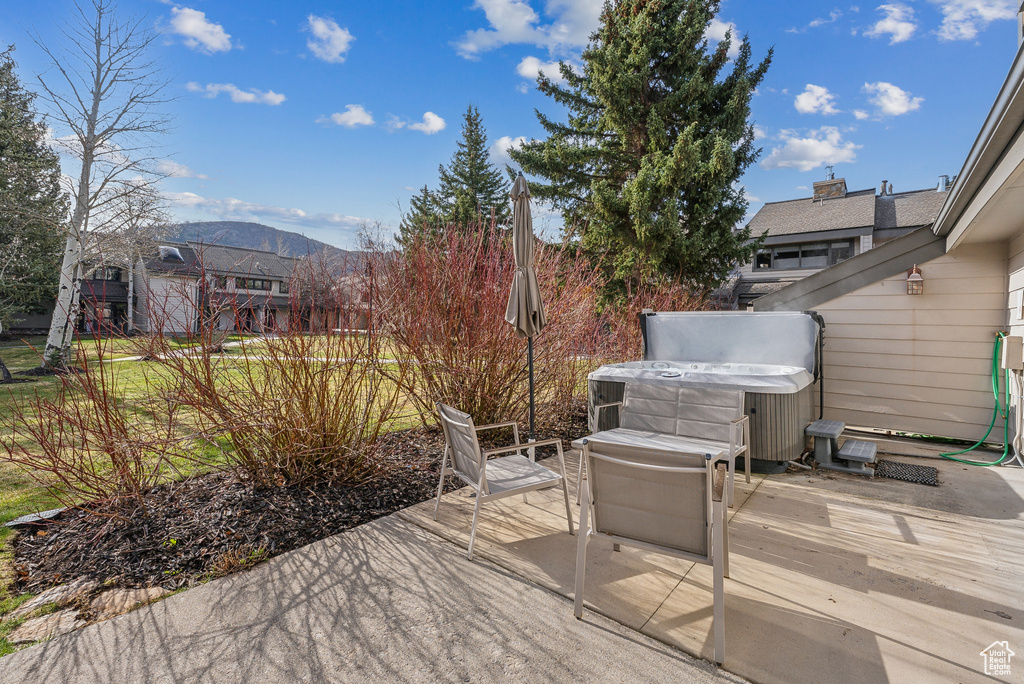 Deck with a hot tub, a mountain view, and a patio area