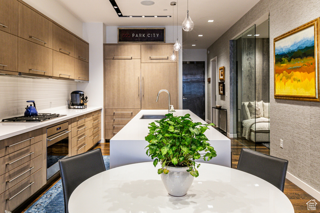 Kitchen featuring hanging light fixtures, an island with sink, dark wood-type flooring, sink, and stainless steel appliances