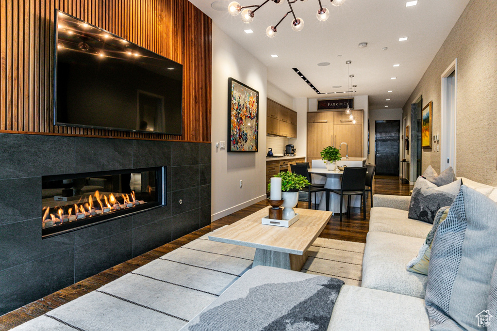 Living room with dark wood-type flooring, a chandelier, sink, and a tile fireplace